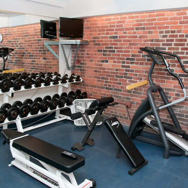 A fitness room with weightlifting equipment and a brick wall